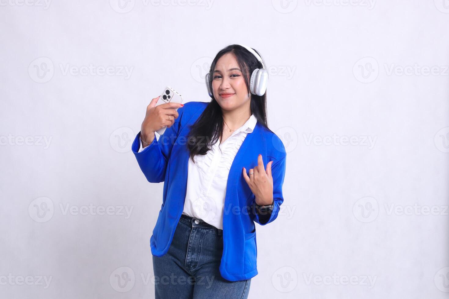 beautiful adult office woman wearing blue formal suit standing smiling to camera while carrying smartphone and headphone while dancing isolated white background. for technology, music, entertainment photo