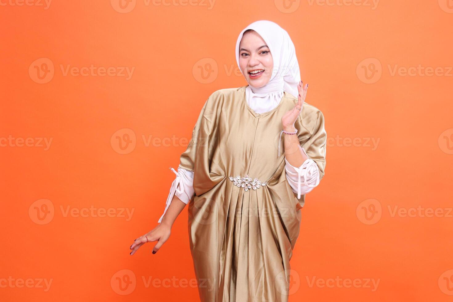 gesture of a beautiful adult indonesia woman, cheerful, palms up and down, wearing a Muslim dress, kaftan, hijab, isolated on an orange background. Fashion, education, promotion concept photo