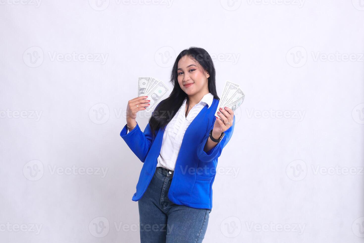 beautiful adult office woman wearing blue formal suit standing smiling to camera holding dollar bills to the right left in front of white background isolation. for transaction, finance, business photo