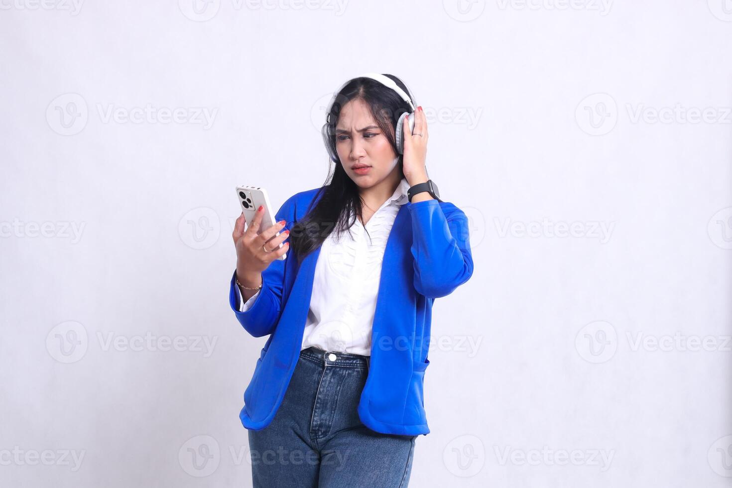 beautiful mature office woman wearing blue formal suit standing angry candid while carrying smartphone cellphone and holding headphone. for technology, lifestyle, music, entertainment content photo