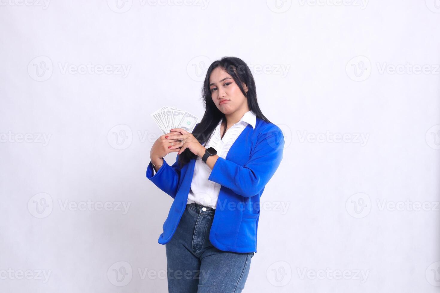 beautiful mature office woman wearing blue formal suit standing pouting to camera both hands holding dollar bill to right isolated white background. for transaction, finance, business content photo