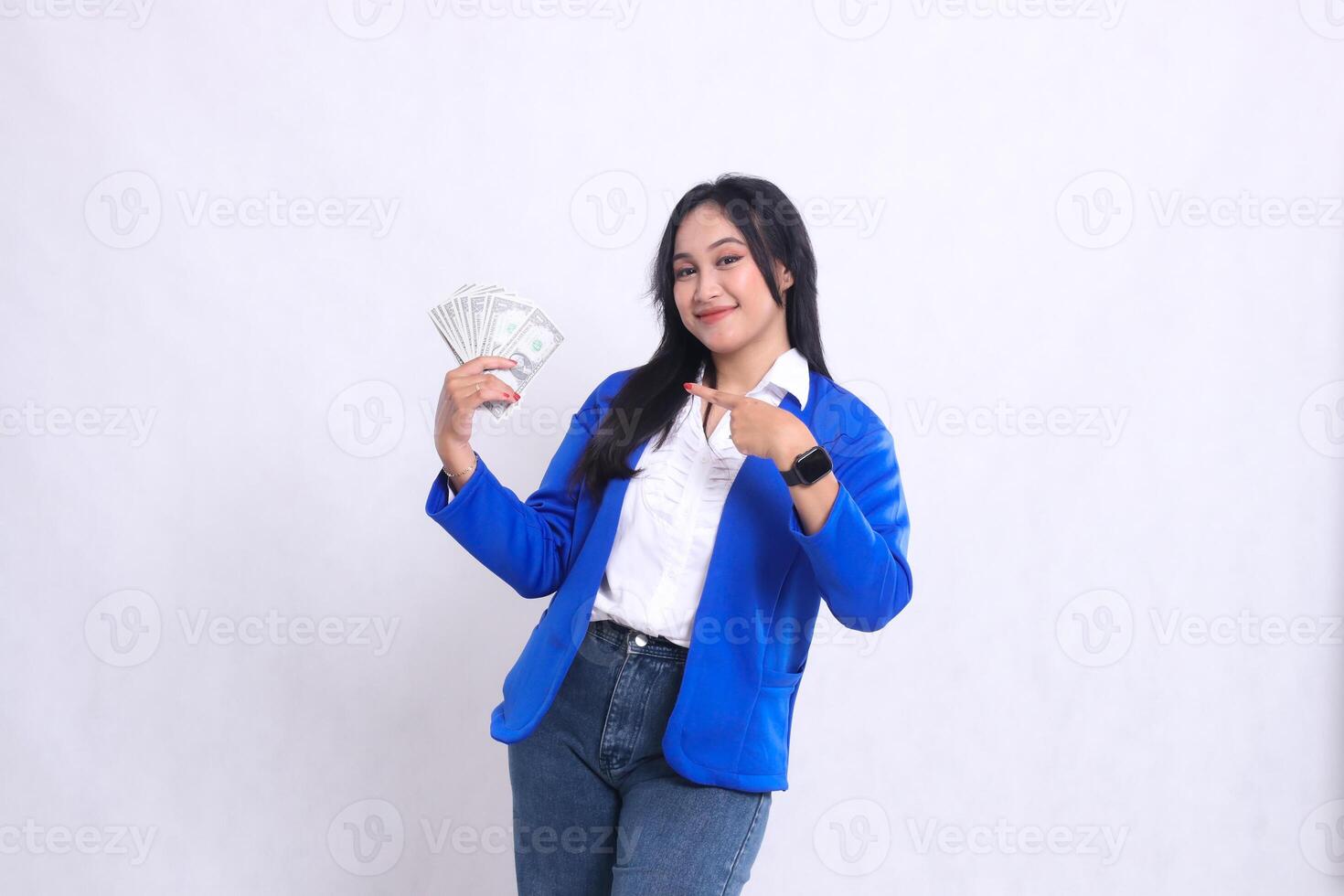 beautiful adult office woman wearing blue formal suit standing smiling to camera holding dollar bill to right and pointing it isolated white background. for transaction, finance, business content photo