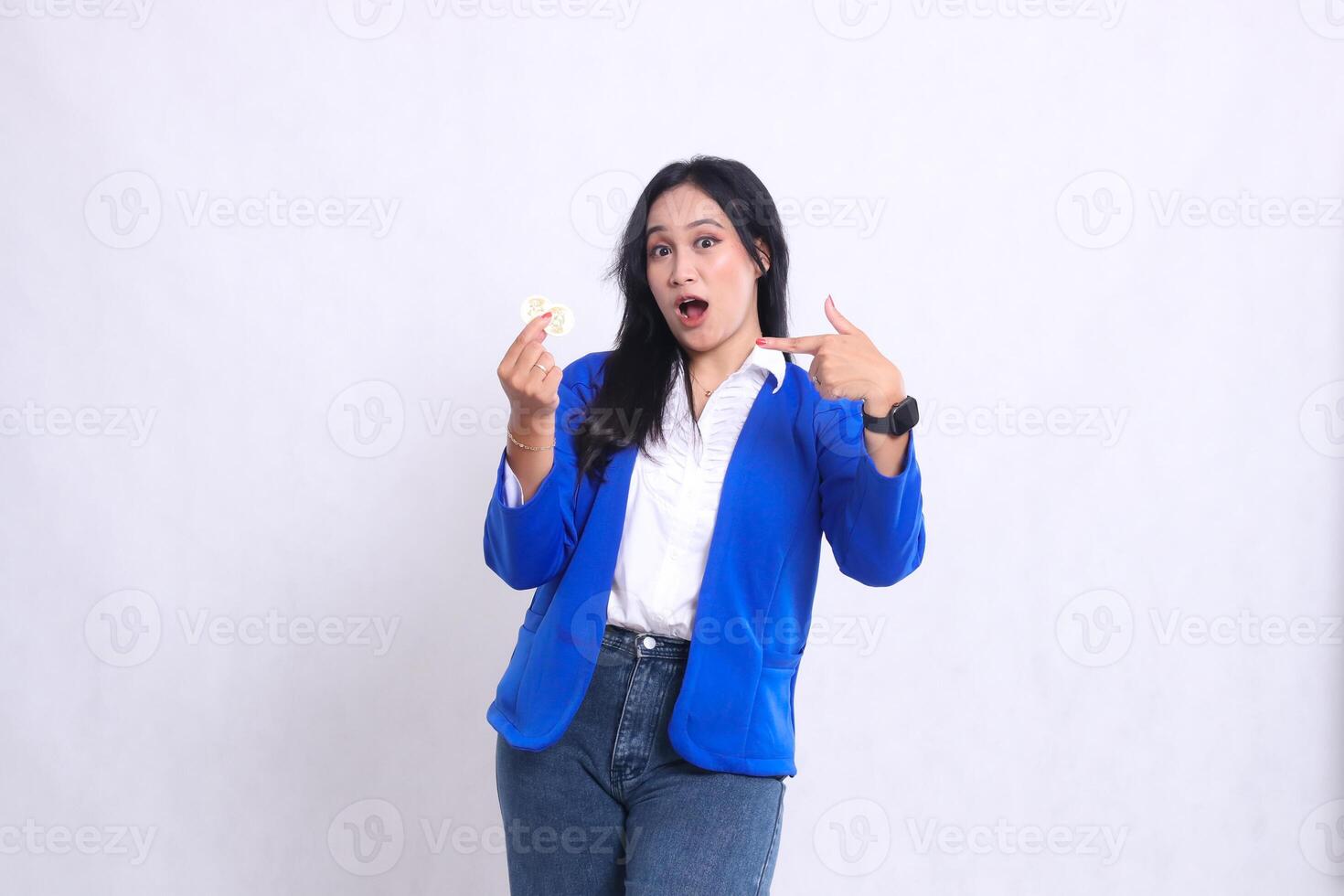 gesture of beautiful mature office woman wearing blue formal suit standing surprised to camera holding bitcoin while pointing at it isolated white background. for transaction content, investment photo