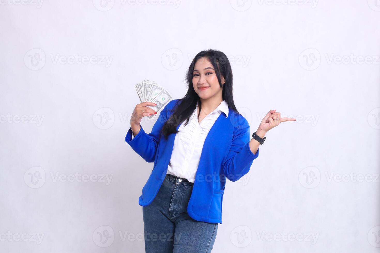 beautiful mature office woman wearing blue formal suit standing smiling to camera holding dollar bill to right and pointing to left isolated white background. for transaction, finance, business photo