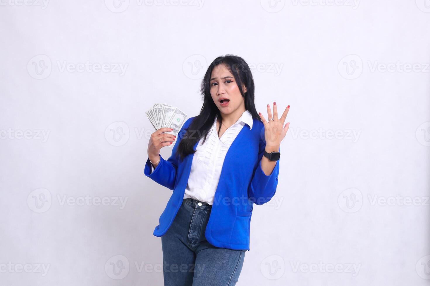 beautiful adult office woman wearing blue formal suit standing surprised to camera holding dollar bill to right and side isolated white background. for transaction, finance, business content photo