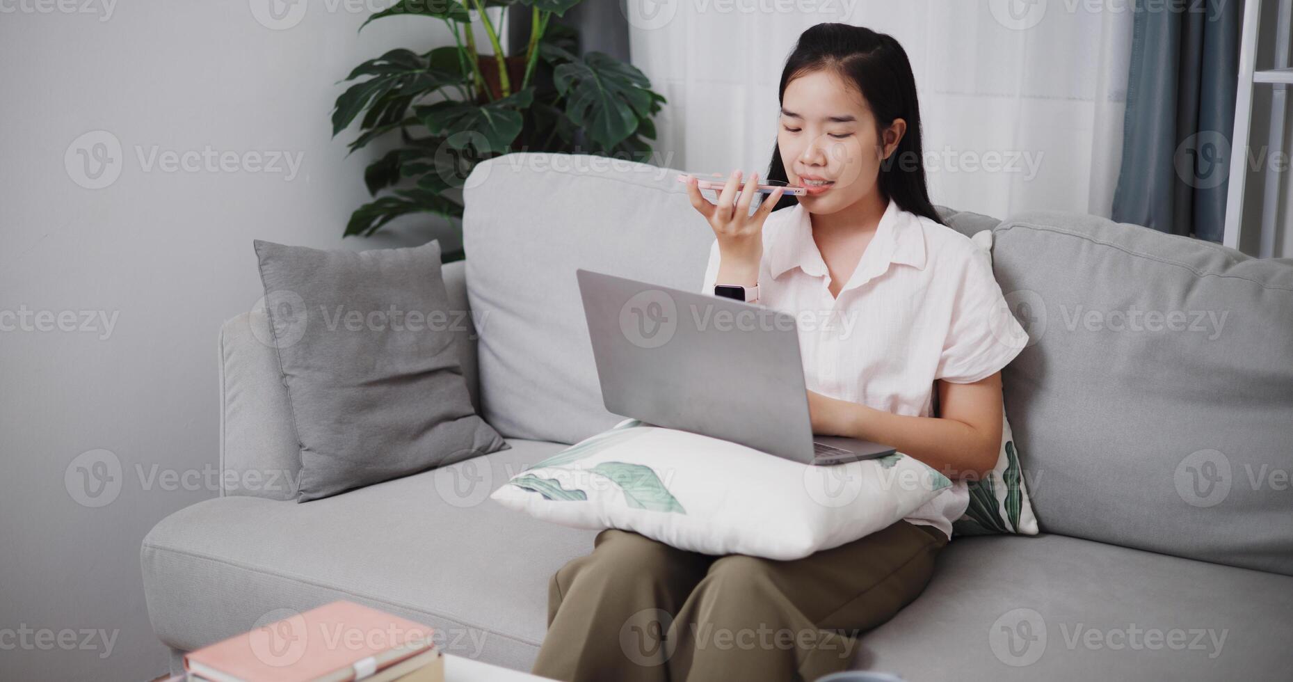 High angle view, Young asian woman recording a message on cell phone while working on laptop in the living room at home ,Lifestyle with device technology, Working from home photo