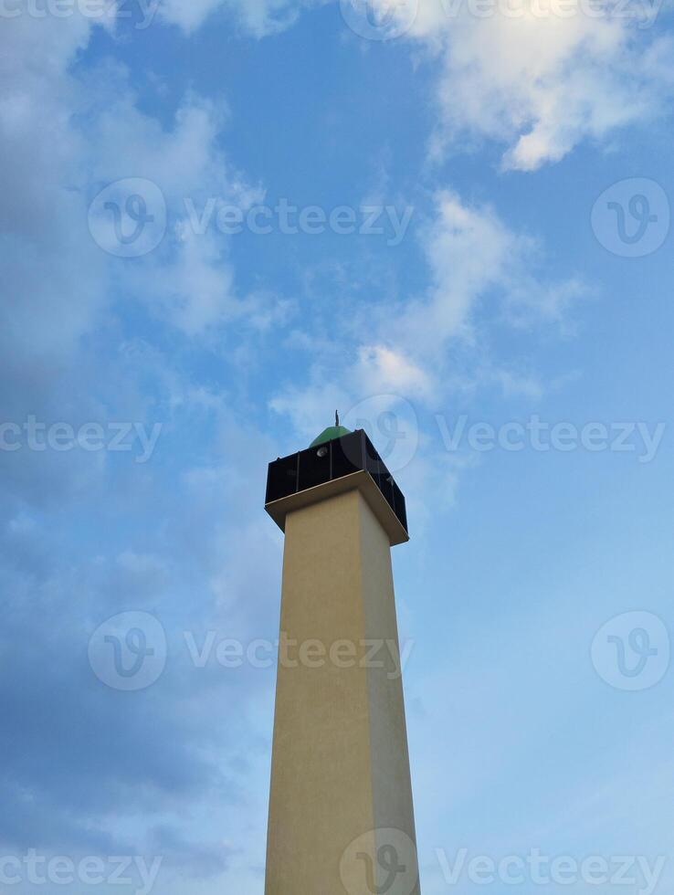 a tall white lighthouse with a green light on top photo