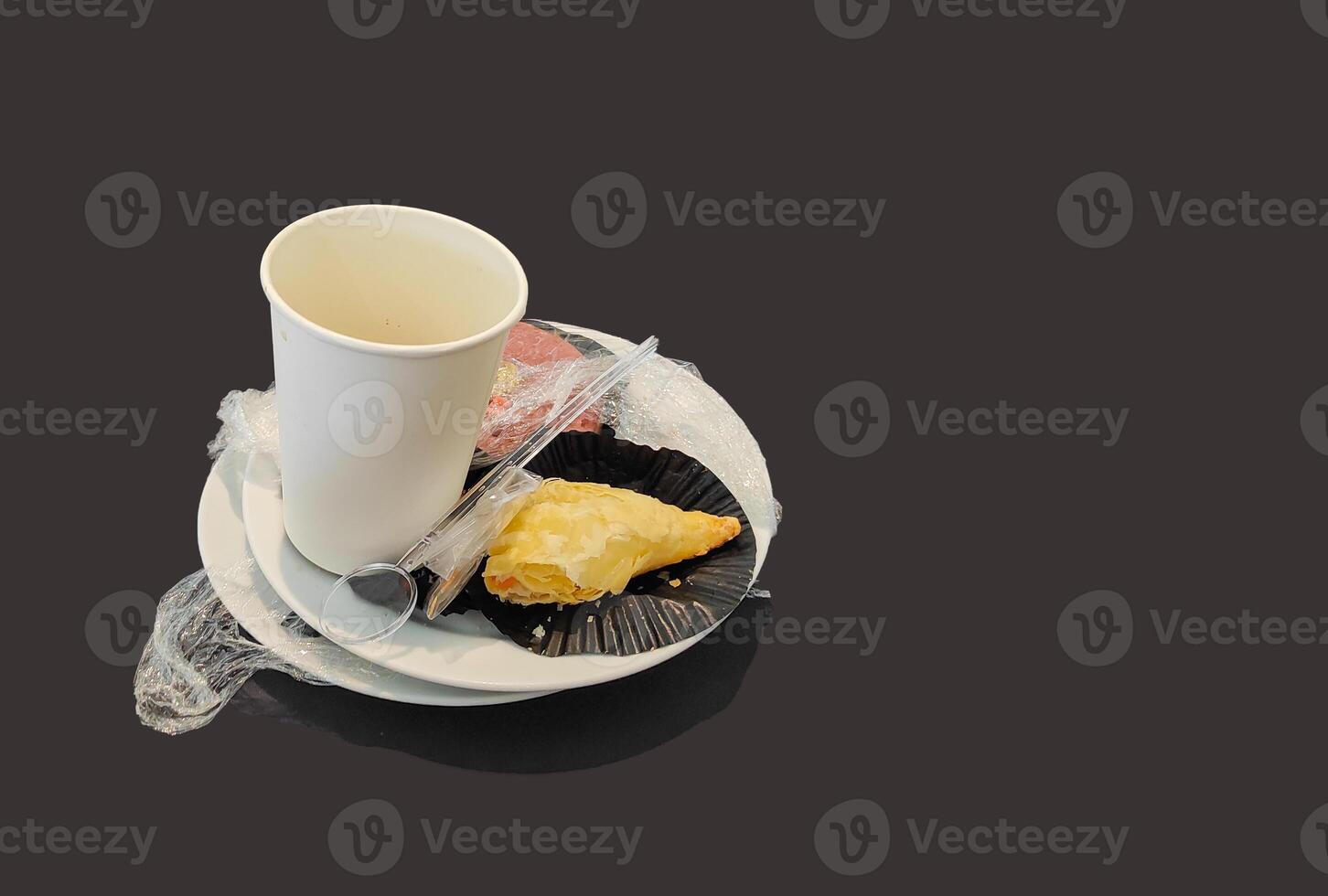 Leftover food on a white plate and empty dirty paper coffee cup on black background. photo