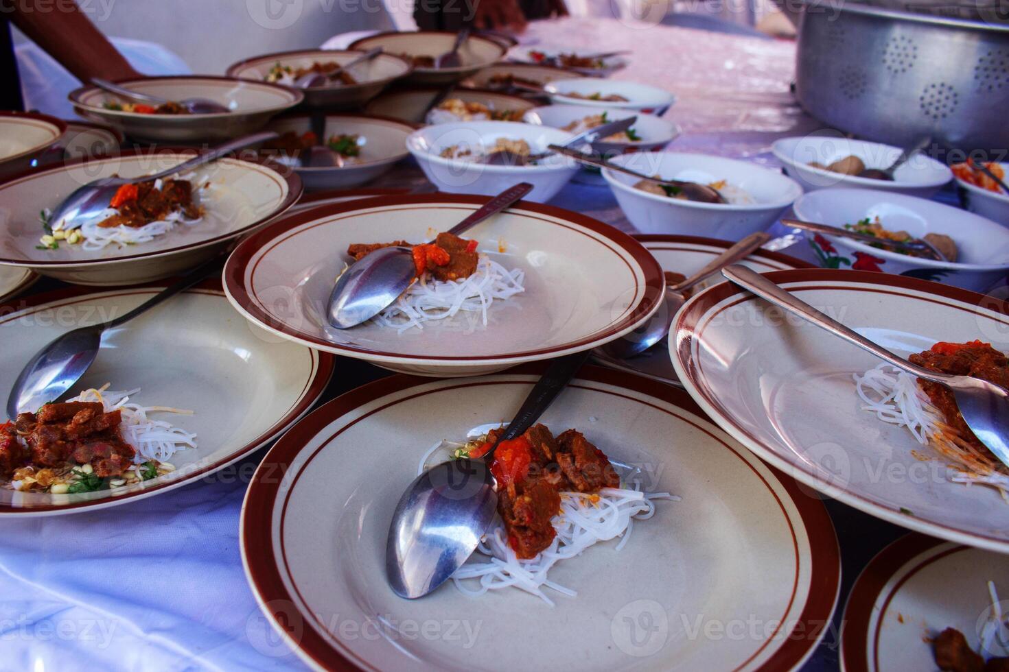 Plates of noodles with toppings ready to be served at a bustling street food stall photo