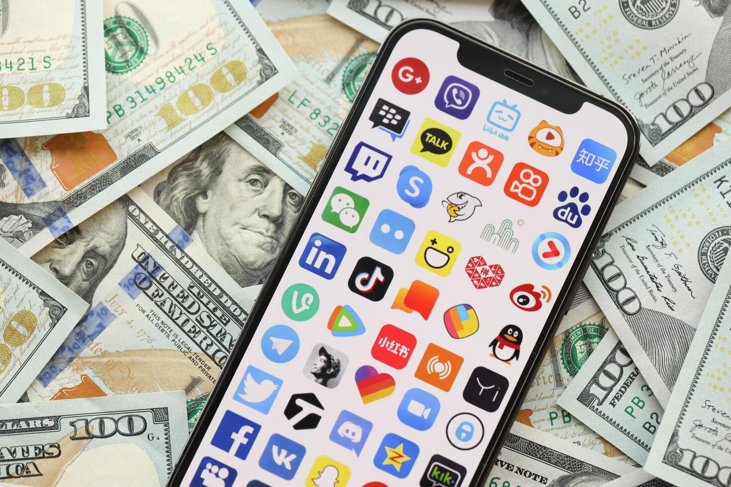 KYIV, UKRAINE - APRIL 1, 2024 Many apps icon on smartphone screen on many usd money bills photo