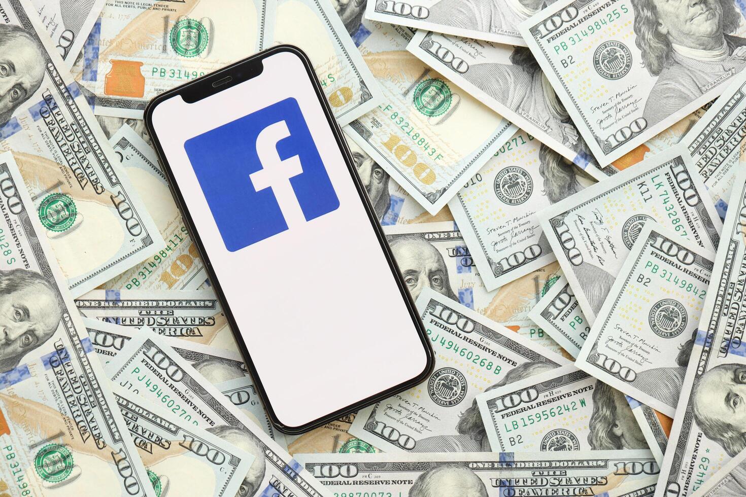KYIV, UKRAINE - APRIL 1, 2024 Facebook icon on smartphone screen on many usd money bills photo