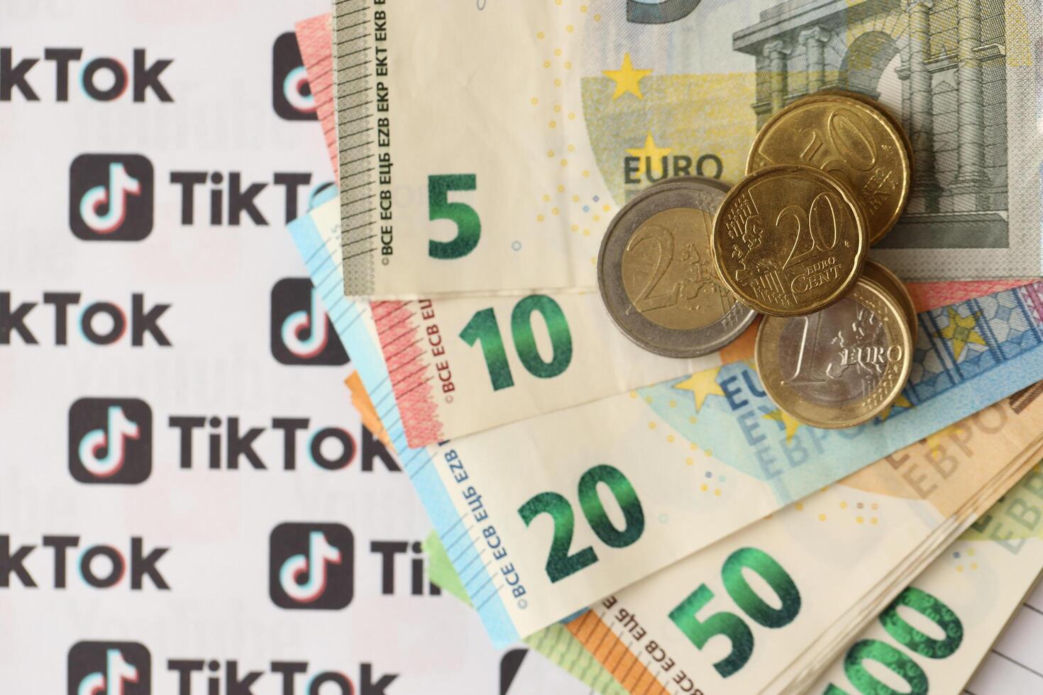 KYIV, UKRAINE - APRIL 20, 2024 TikTok logo and many euro money bills. Symbol of famous social network platform and european currency banknotes photo