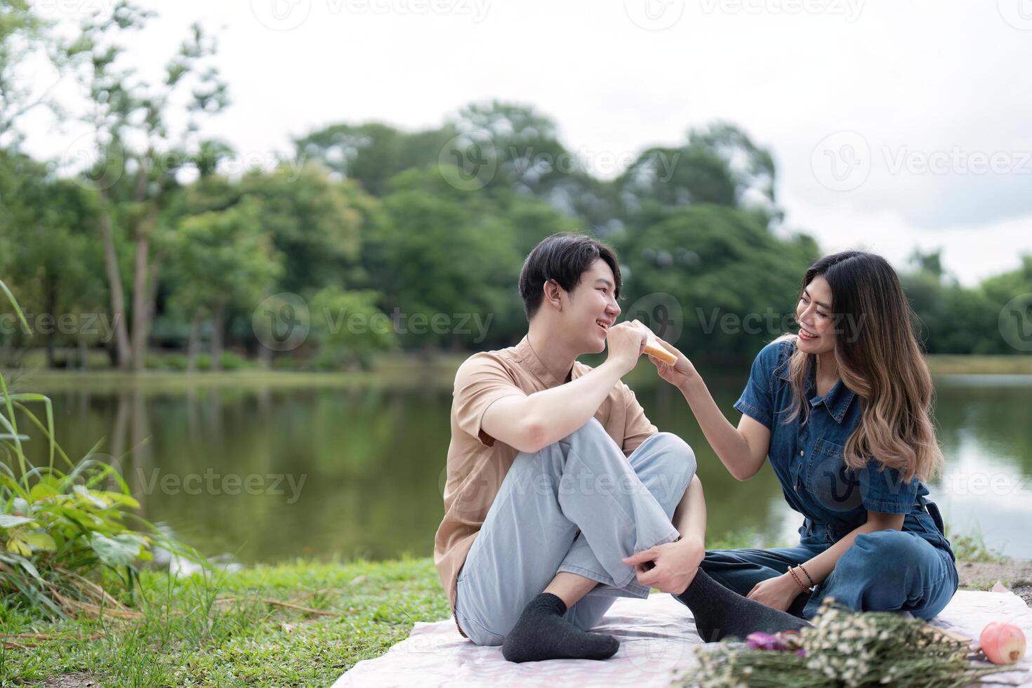 Romantic Couple Enjoying a Picnic by the Lake in a Serene Park Setting with Lush Greenery and Tranquil Waters photo