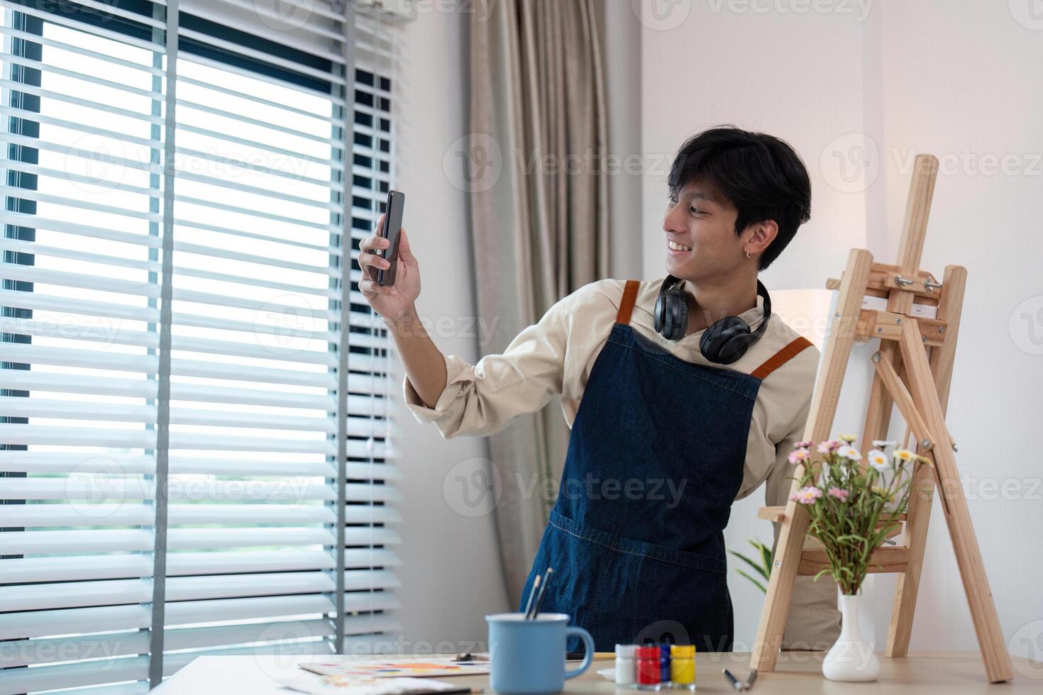 Young Artist Taking a Selfie in Studio with Easel and Art Supplies, Wearing Apron and Headphones photo