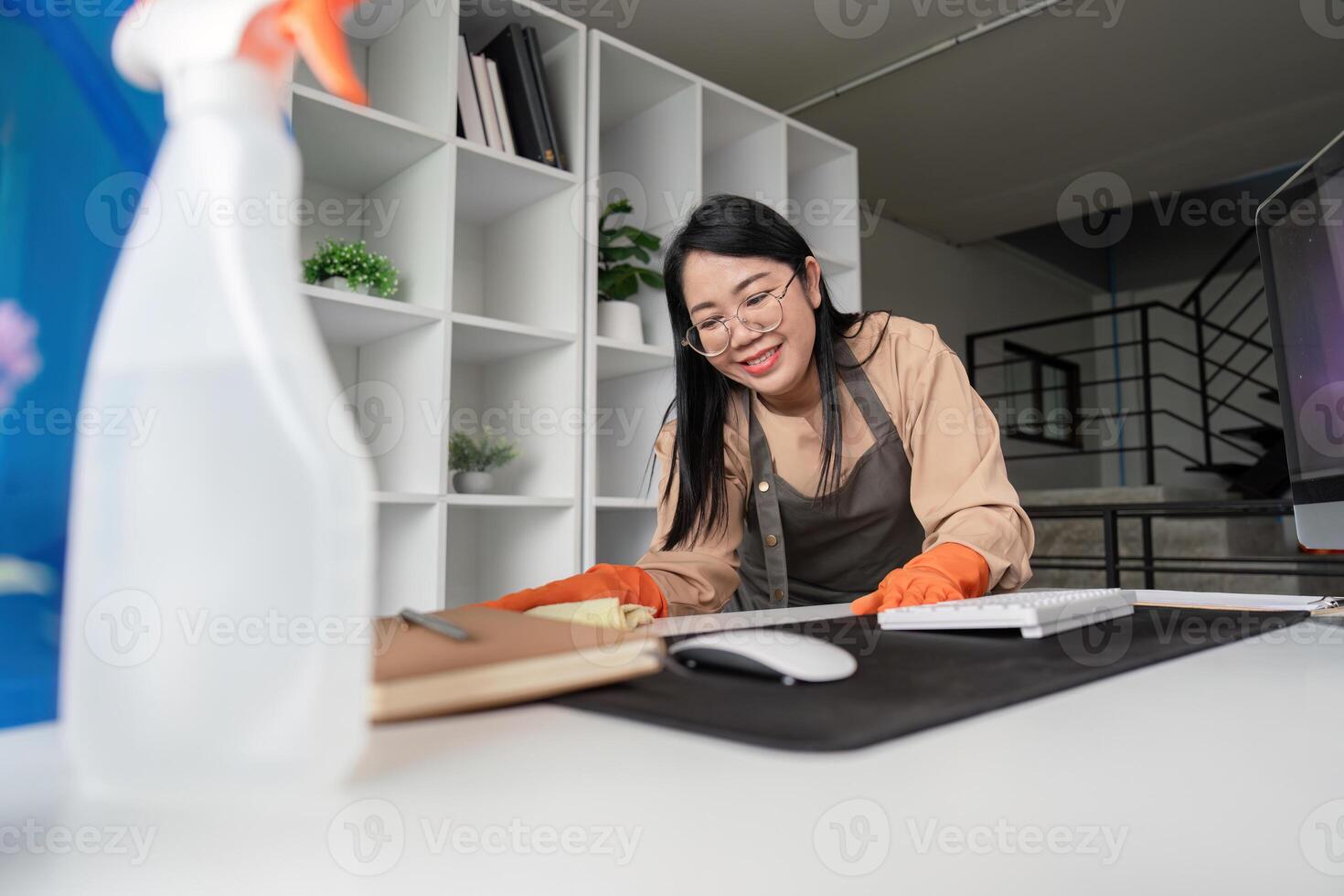 Smiling Maid Housekeeper Cleaning Modern Office Desk with Spray Bottle and Cloth in Contemporary Workspace photo