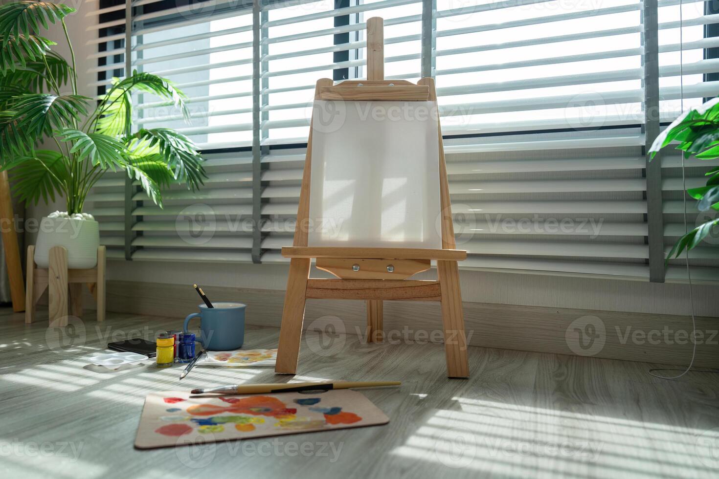 Sunlit Artist's Studio with Wooden Easel, Paints, and Brushes by Large Window Blinds photo