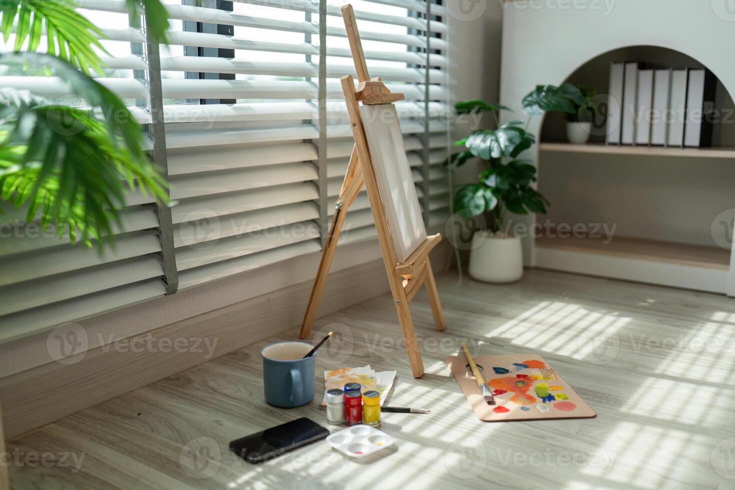 Cozy Art Studio with Easel and Painting Supplies in Sunlit Room with Plants and Bookshelf photo