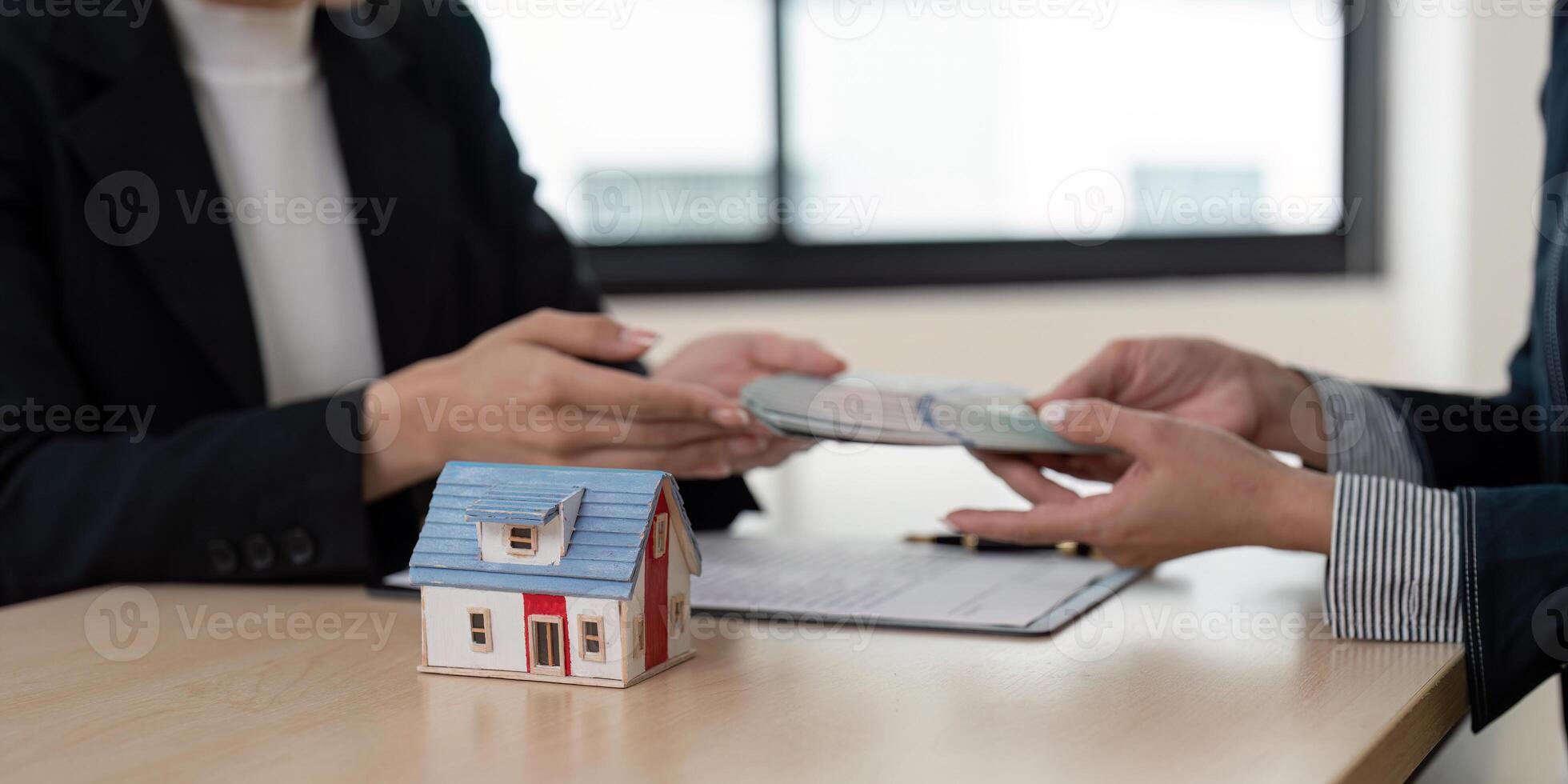 Real Estate Agent Handing Over Money for Property Sale with House Model on Desk in Office Setting photo