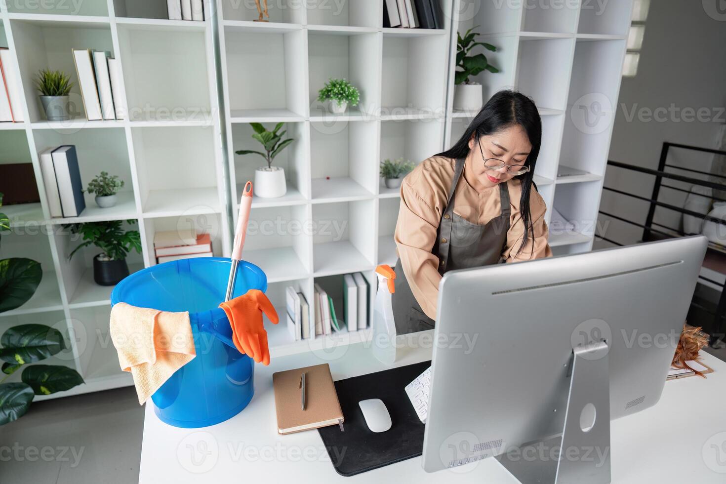 Professional Maid Housekeeper Cleaning Modern Office Space with Computer and Bookshelves in Background photo