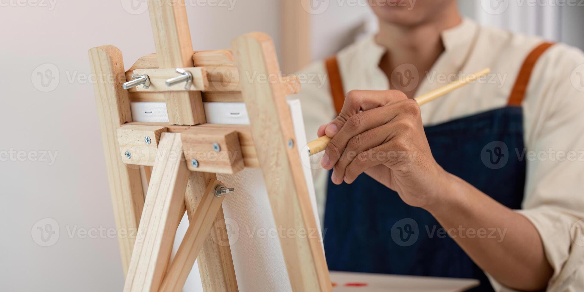 Artist Painting on Canvas with Wooden Easel in Studio, Close Up of Hand Holding Brush, Creative Process in Art Workshop photo