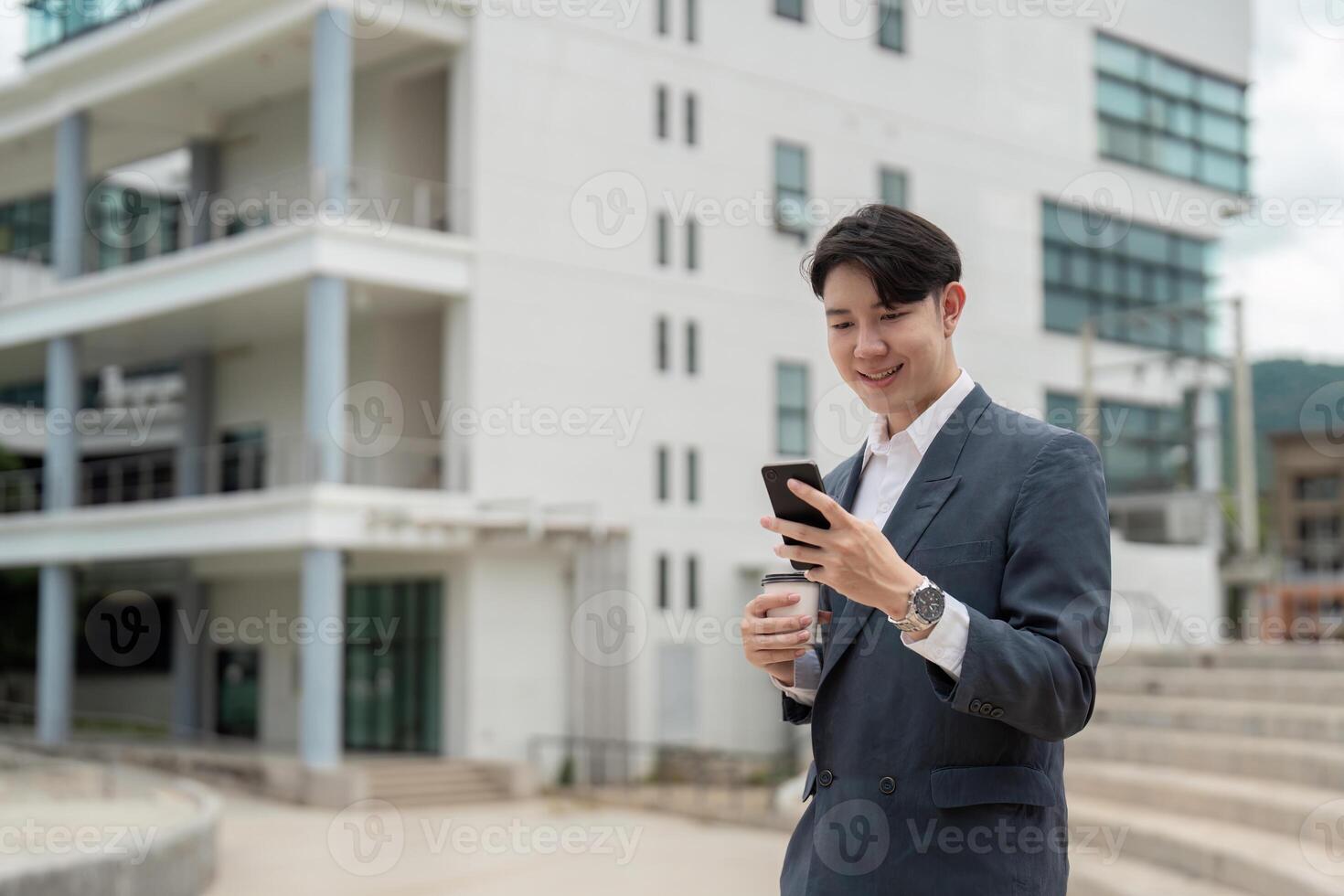 Young Professional Man in Suit Using Smartphone and Holding Coffee Cup Outside Modern Office Building photo