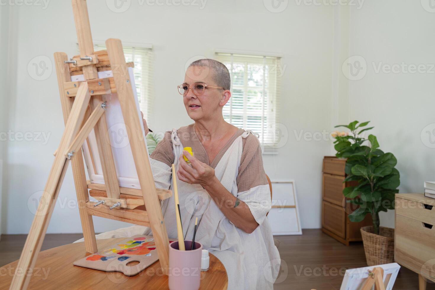 Senior Woman Painting on Canvas in Bright Studio with Natural Light and Wooden Easel photo