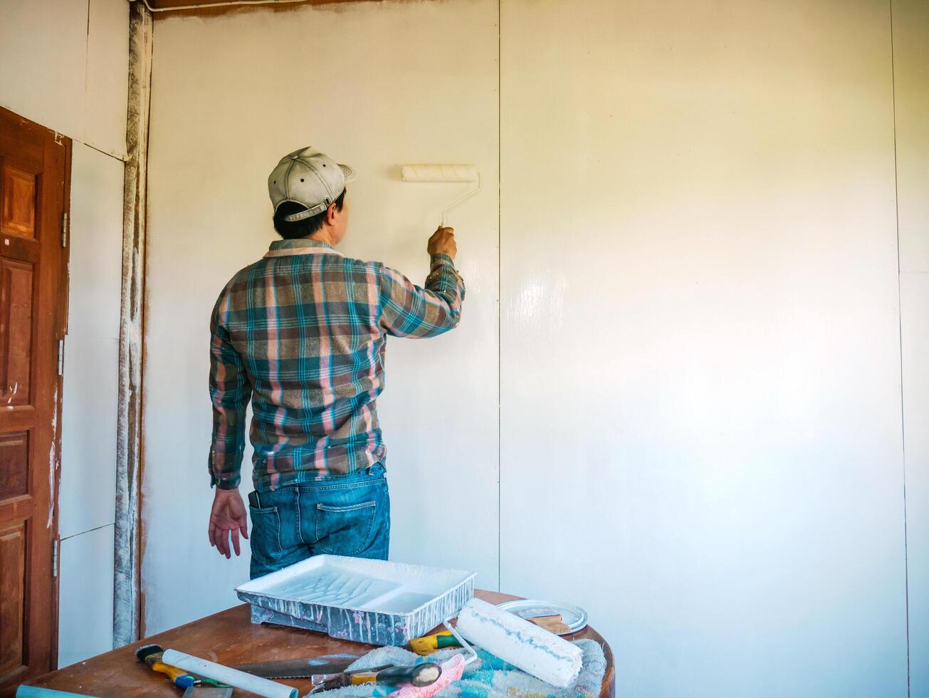 Back view of Workers painter are painting the wooden walls of the room white with paint roller,improvement home interior concept. photo