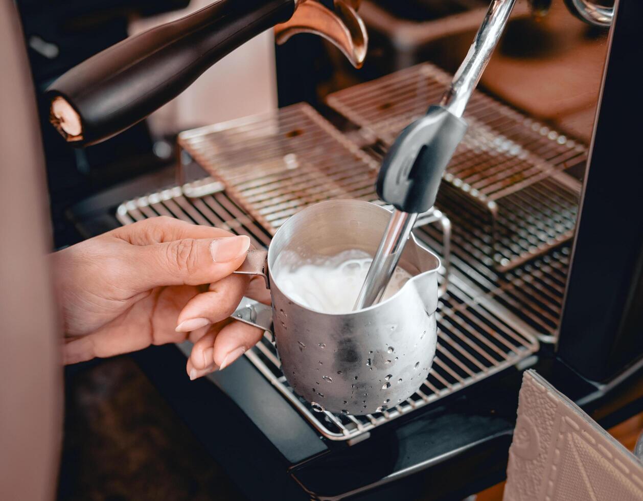 Close-up of Barista hand using high-pressure steam-operated milk frother to prepare a cappuccino and latte coffee milk photo