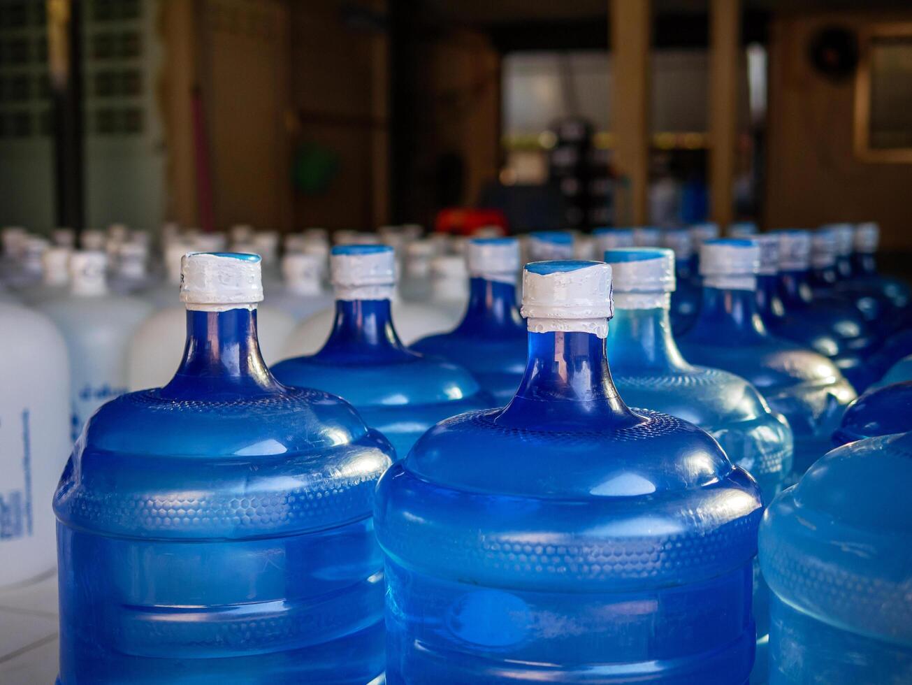 Many blue gallons and white gallon of drinking water are lined up in a drinking water production plant. photo