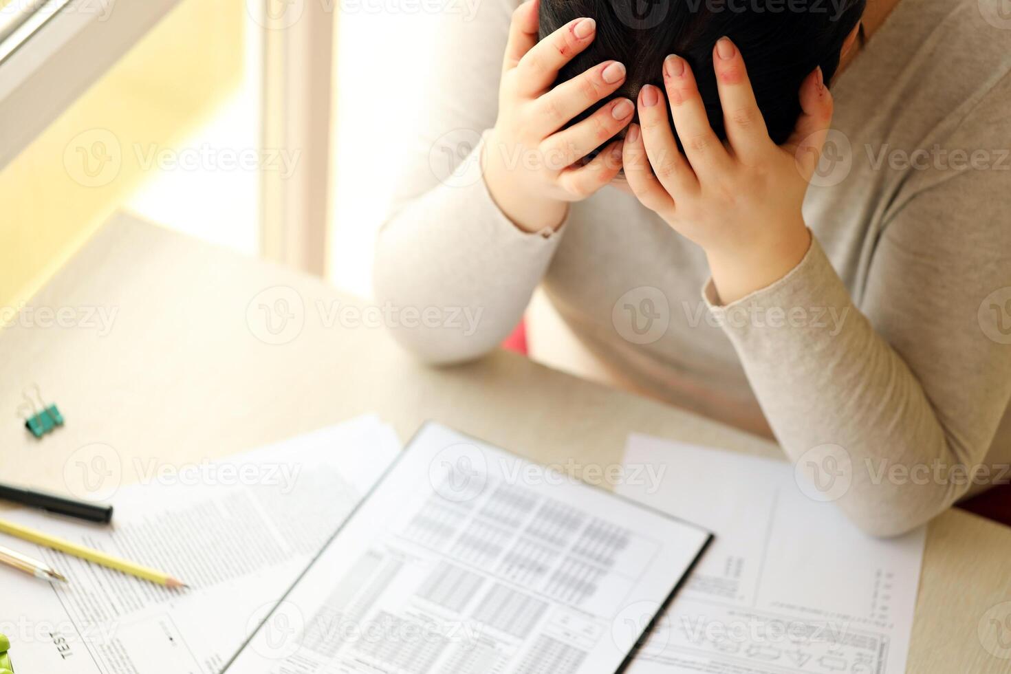 Sad female student testing in exercise and fill exam paper sheet with pencil at school test room photo