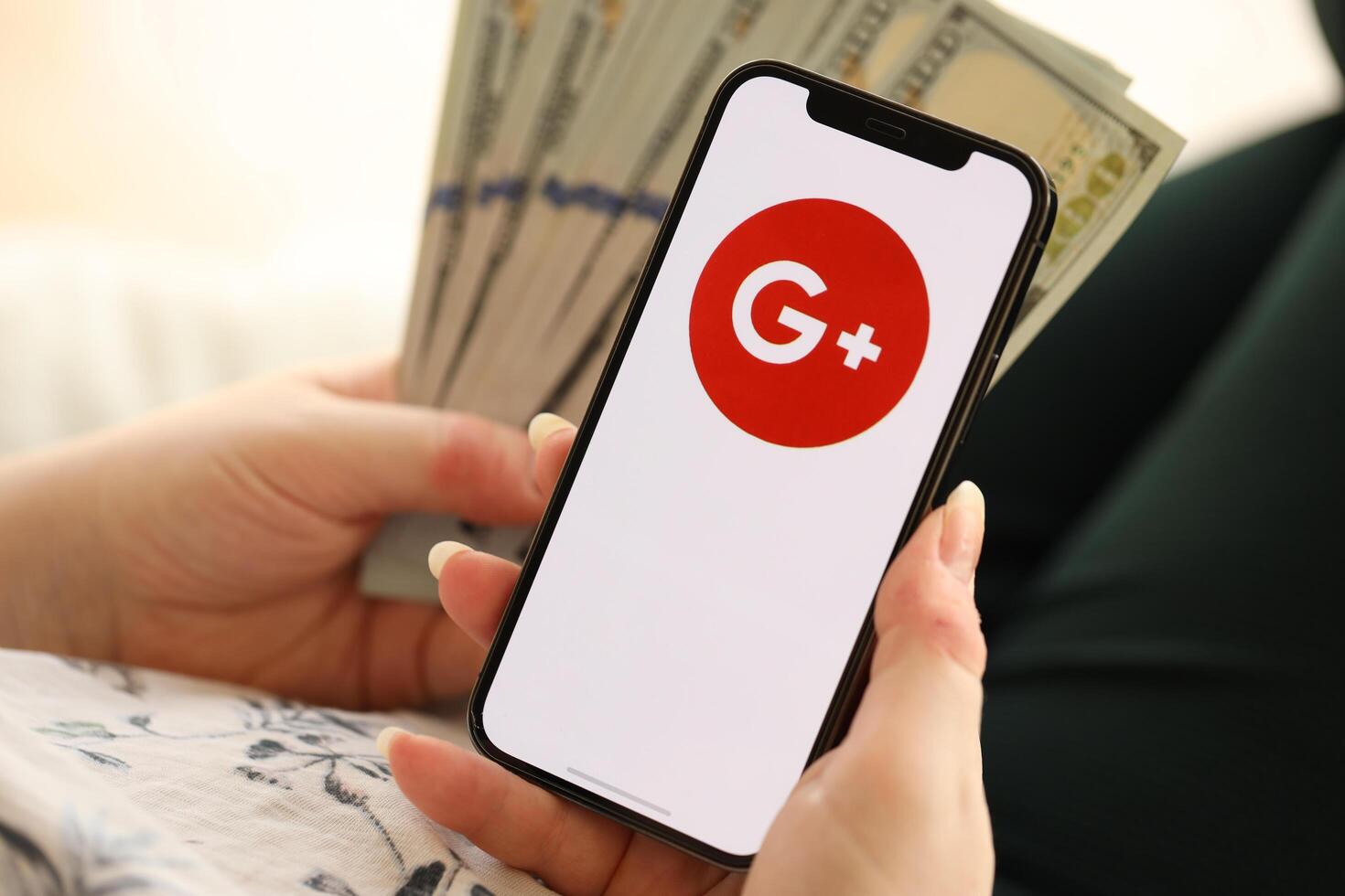 KYIV, UKRAINE - APRIL 1, 2024 Google Plus icon on smartphone screen and money in female hand photo