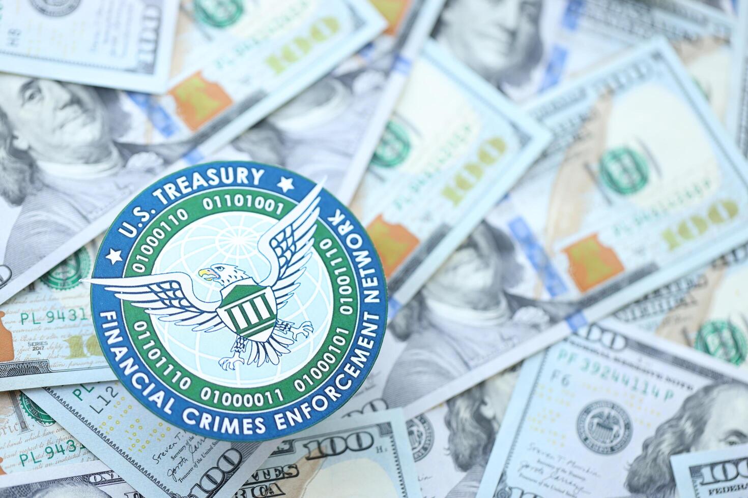 KYIV, UKRAINE - JUNE 26, 2024 U.S. Treasury Financial Crimes Enforcement Network coat of arms on big amount of US dollar banknotes photo
