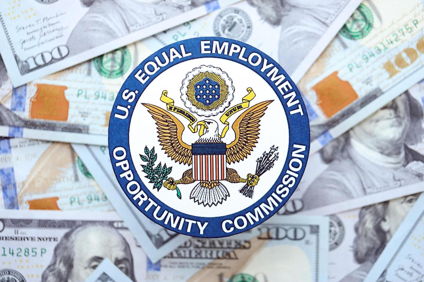 KYIV, UKRAINE - JUNE 26, 2024 U.S. Equal Employment Opportunity Commission coat of arms on big amount of US dollar banknotes photo