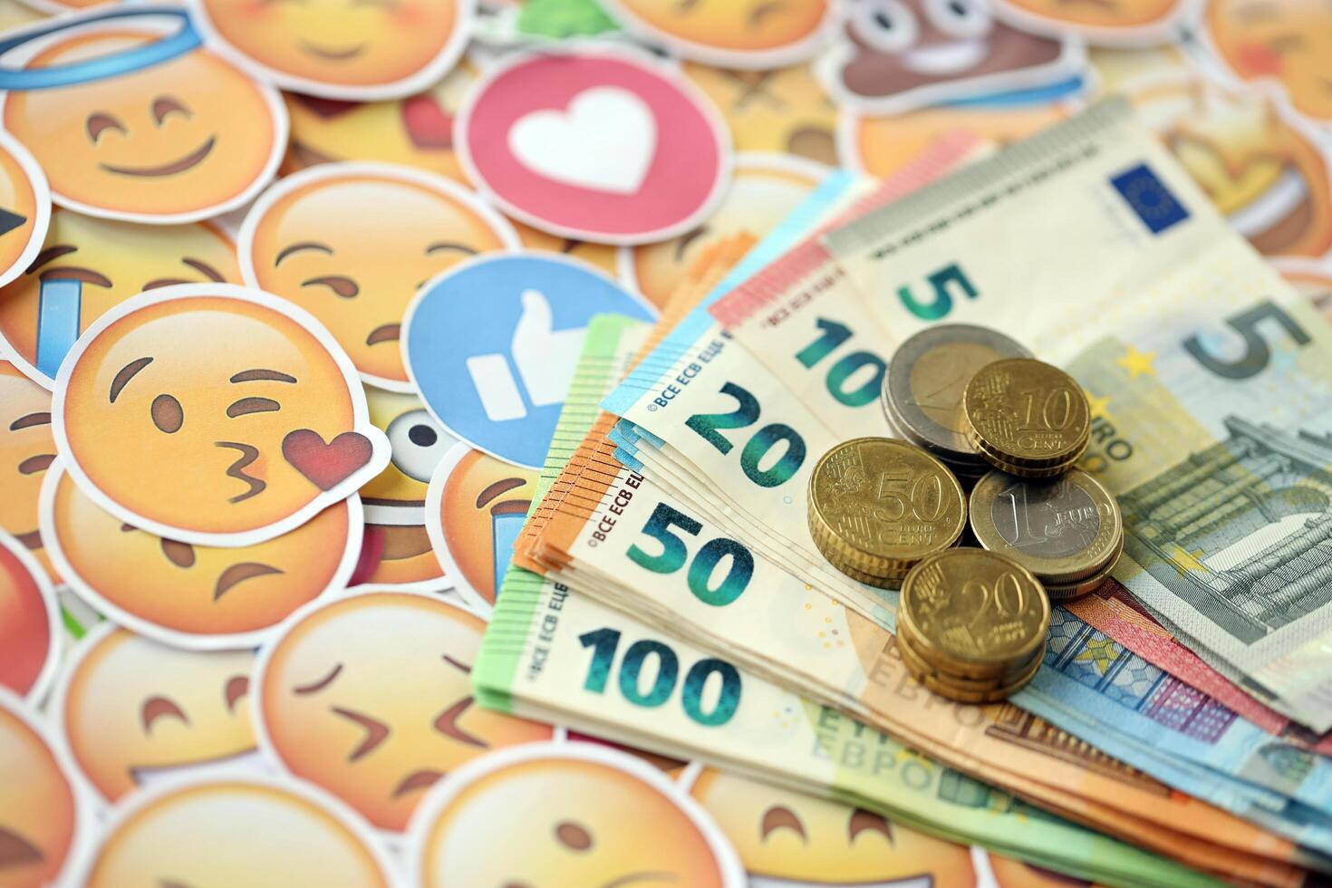 KYIV, UKRAINE - APRIL 20, 2024 European euro money and large set of stickers with Emoji yellow faces. The concept of smm, smo paid service for boost in social media photo