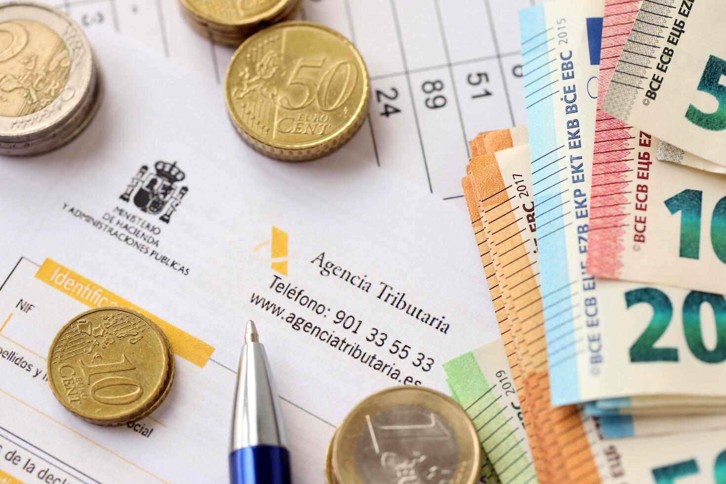 KYIV, UKRAINE - APRIL 20, 2024 Agencia Tributaria logo from blank tax form and many euro banknotes on office table photo