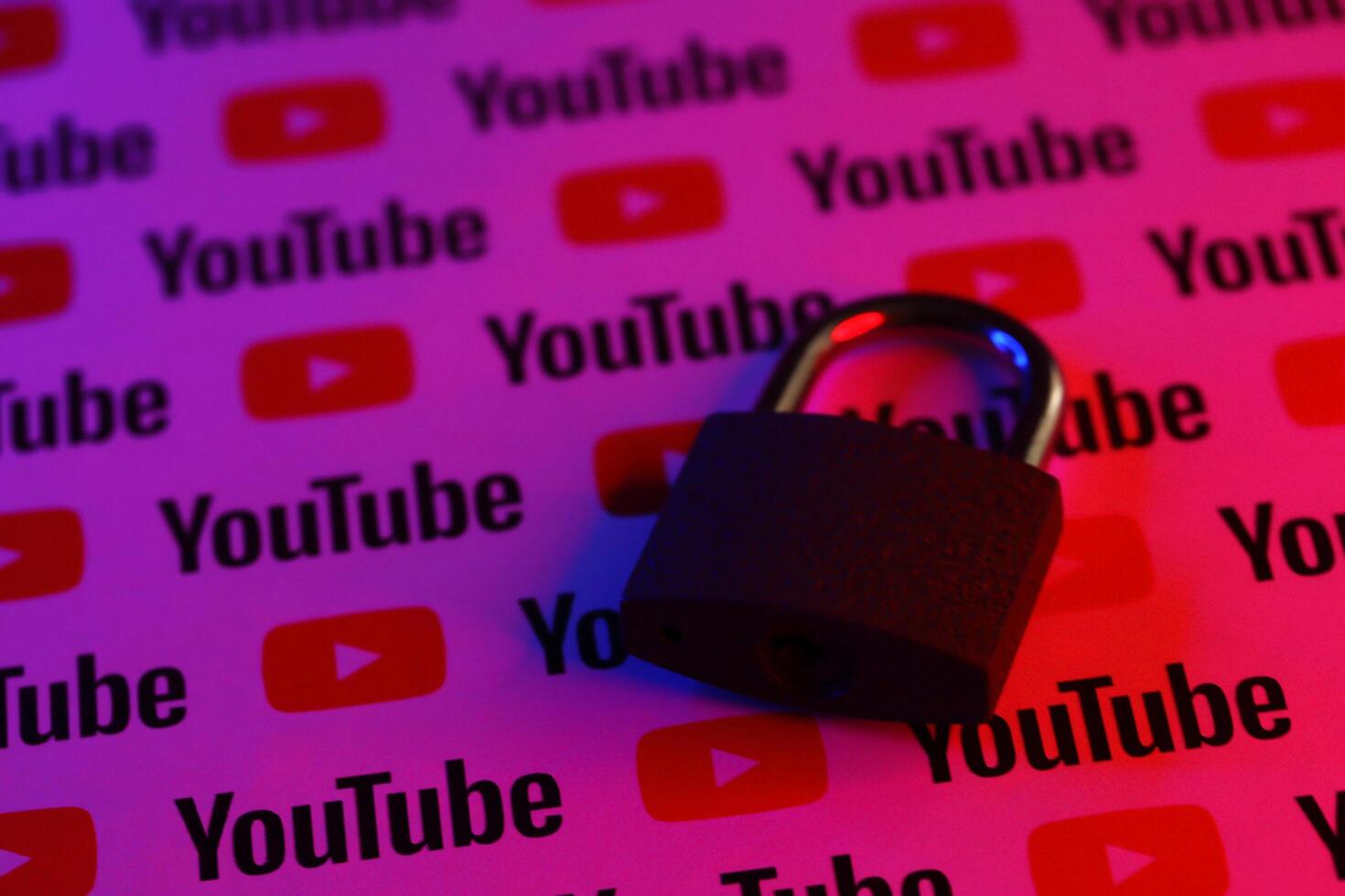 KYIV, UKRAINE - NOVEMBER 27, 2023 Locked small lock on many Youtube logotypes in red and blue light photo