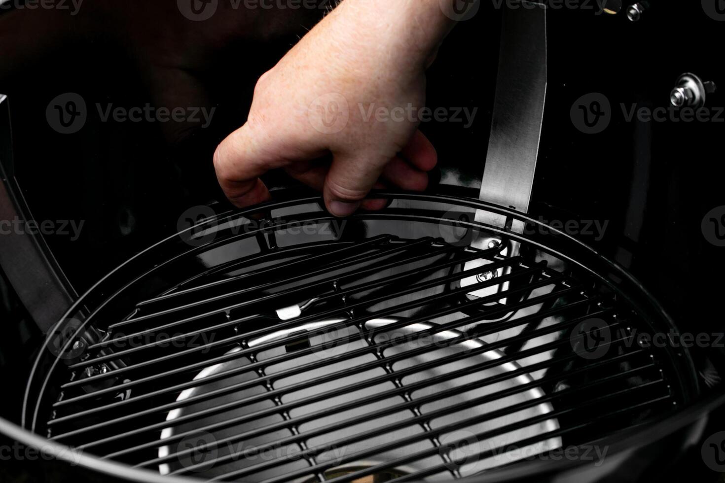 A close up of a hand setting up a black barbecue grill for a summer cookout, highlighting outdoor cooking preparation photo