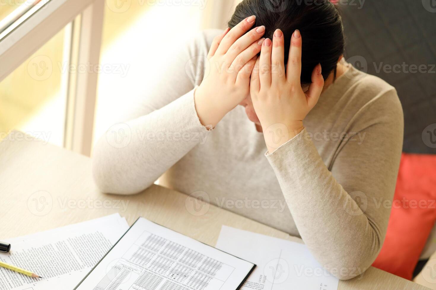 Sad female student testing in exercise and fill exam paper sheet with pencil at school test room photo