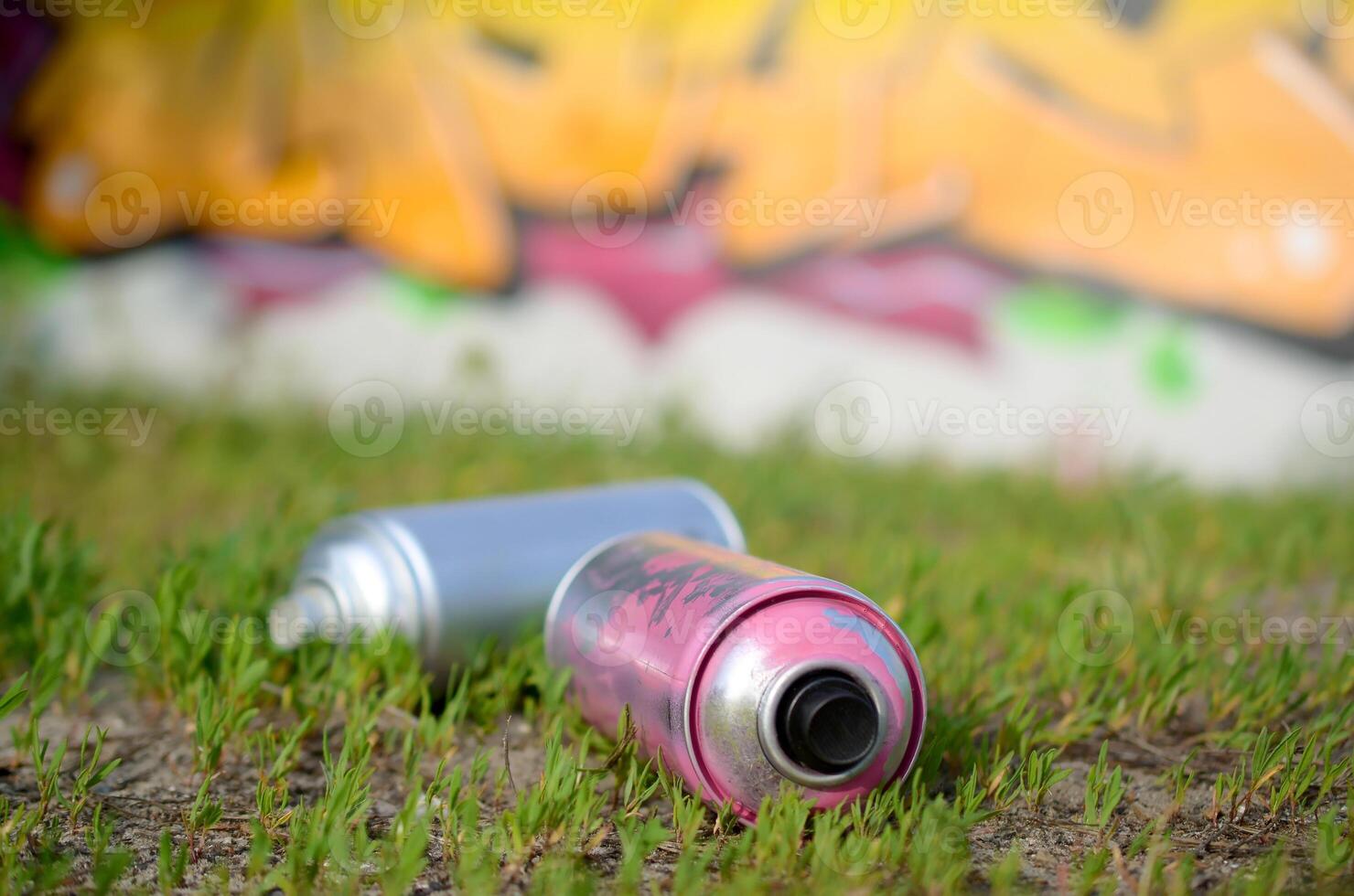 Several used spray cans with paint and caps for spraying paint under pressure on grass near the painted wall in colored graffiti photo