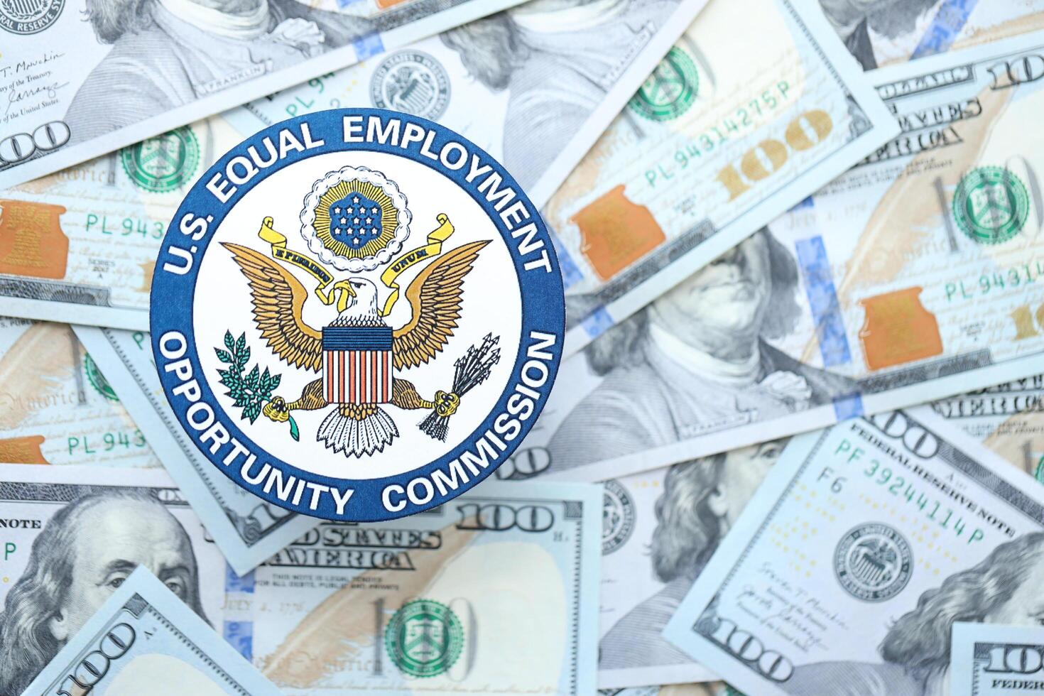 KYIV, UKRAINE - JUNE 26, 2024 U.S. Equal Employment Opportunity Commission coat of arms on big amount of US dollar banknotes photo
