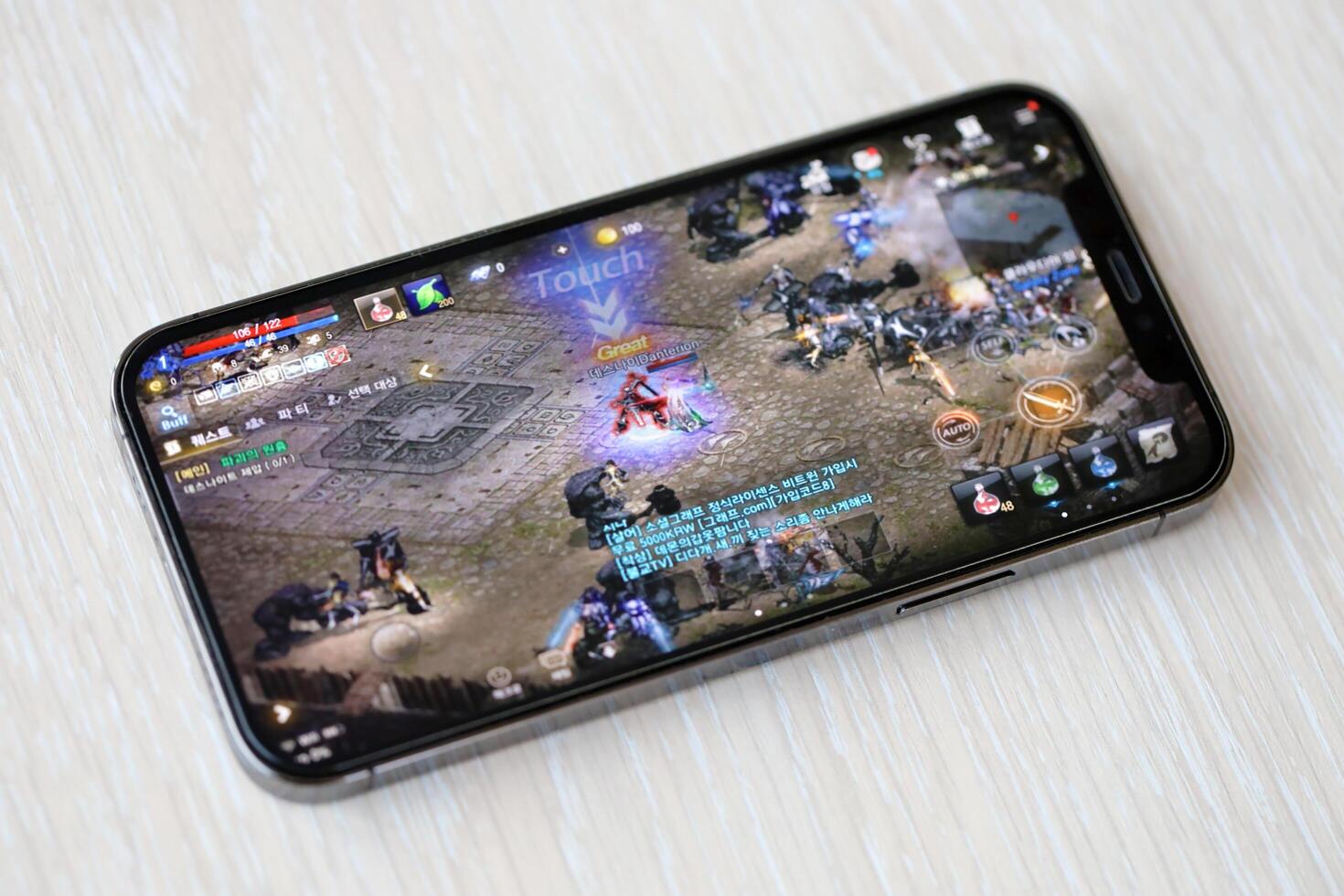 Lineage M mobile iOS game on iPhone 15 smartphone screen on wooden table during mobile gameplay photo