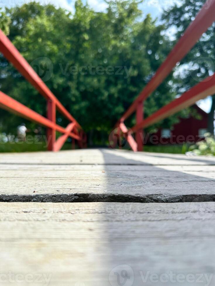 The empty wooden brown bridge top with blur background of green tree, red railing and blue sky. Exuberant image. photo