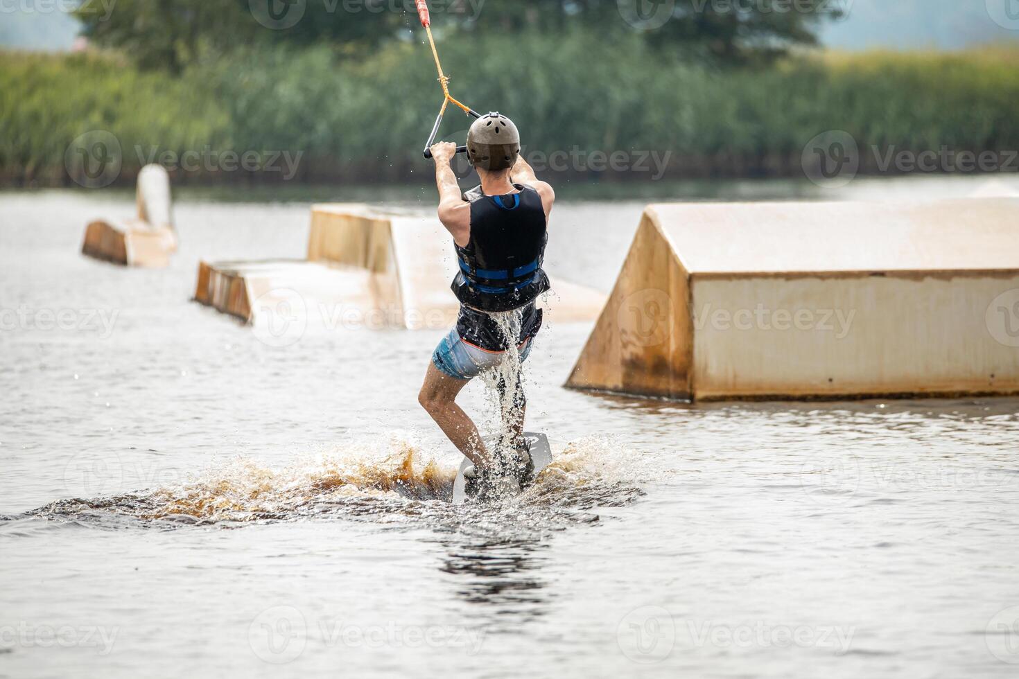 Ypung man wakeboarding and doing different board tricks Wake boarding sportsman man jumping high wake boarding raley trick with huge water splash in the cable park photo