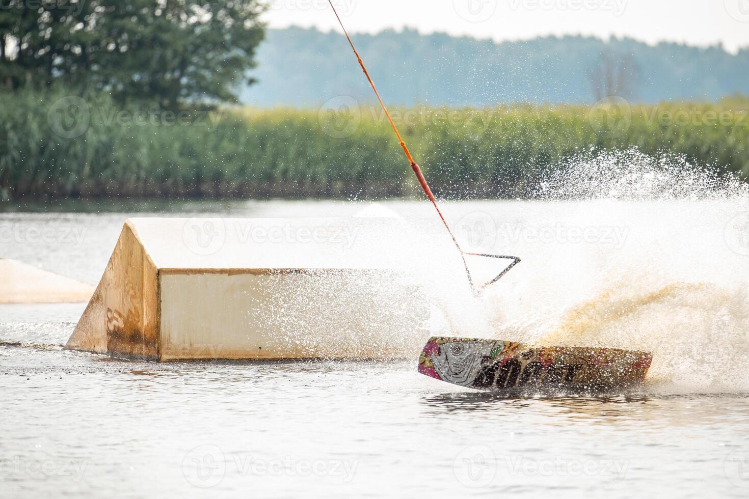 Ypung man wakeboarding and doing different board tricks Wake boarding sportsman man jumping high wake boarding raley trick with huge water splash in the cable park photo