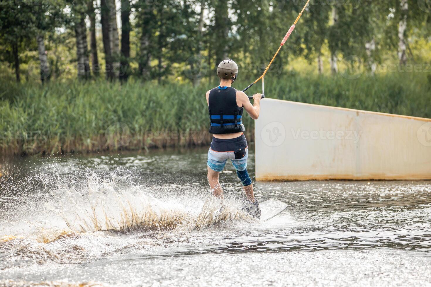 Ypung man wakeboarding and doing different board tricks Wake boarding sportsman man jumping high wake boarding raley trick with huge water splash in the cable park photo