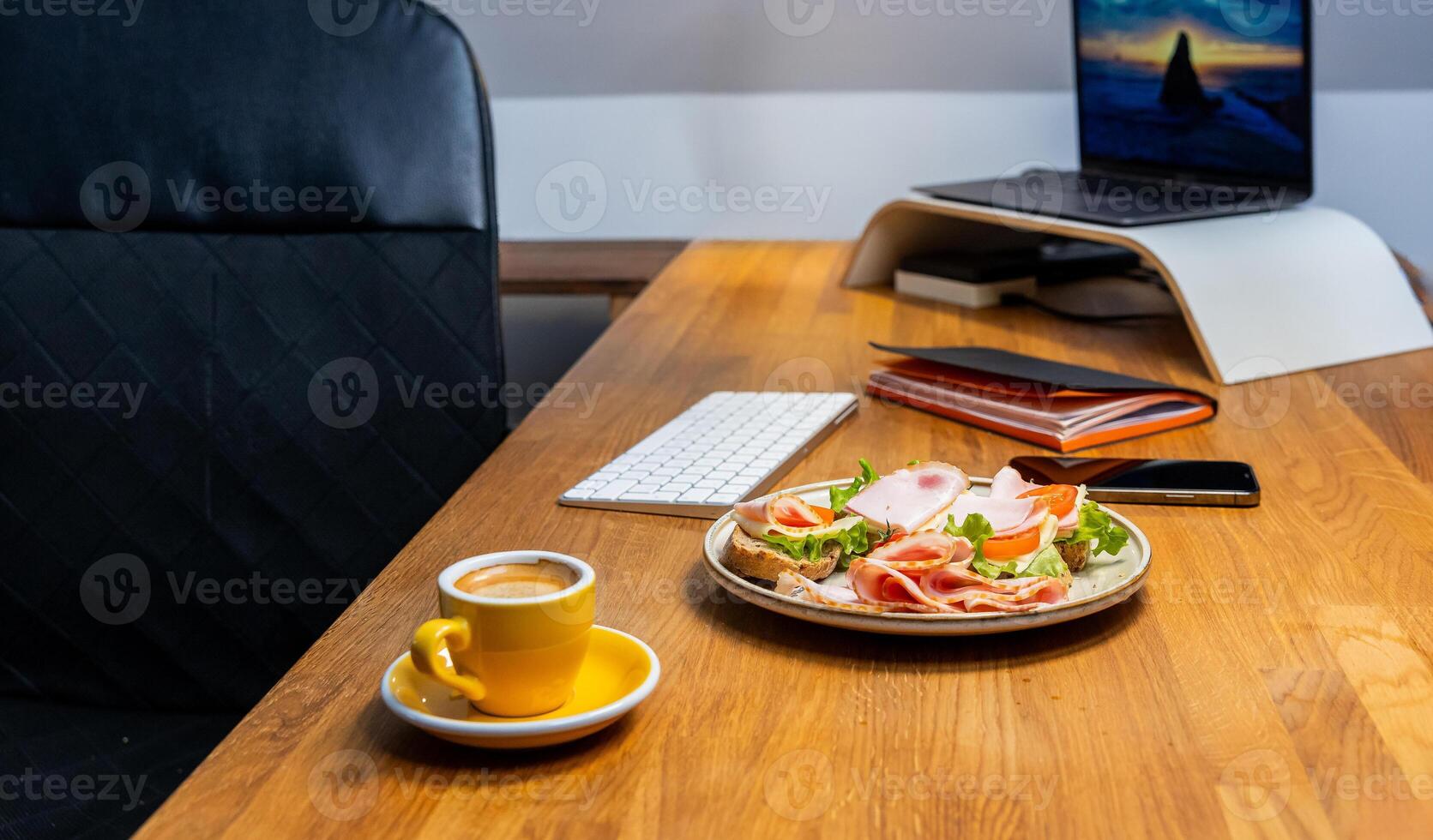 Modern office desk setup with gourmet sandwich, espresso, smartphone and laptop for a productive workday photo