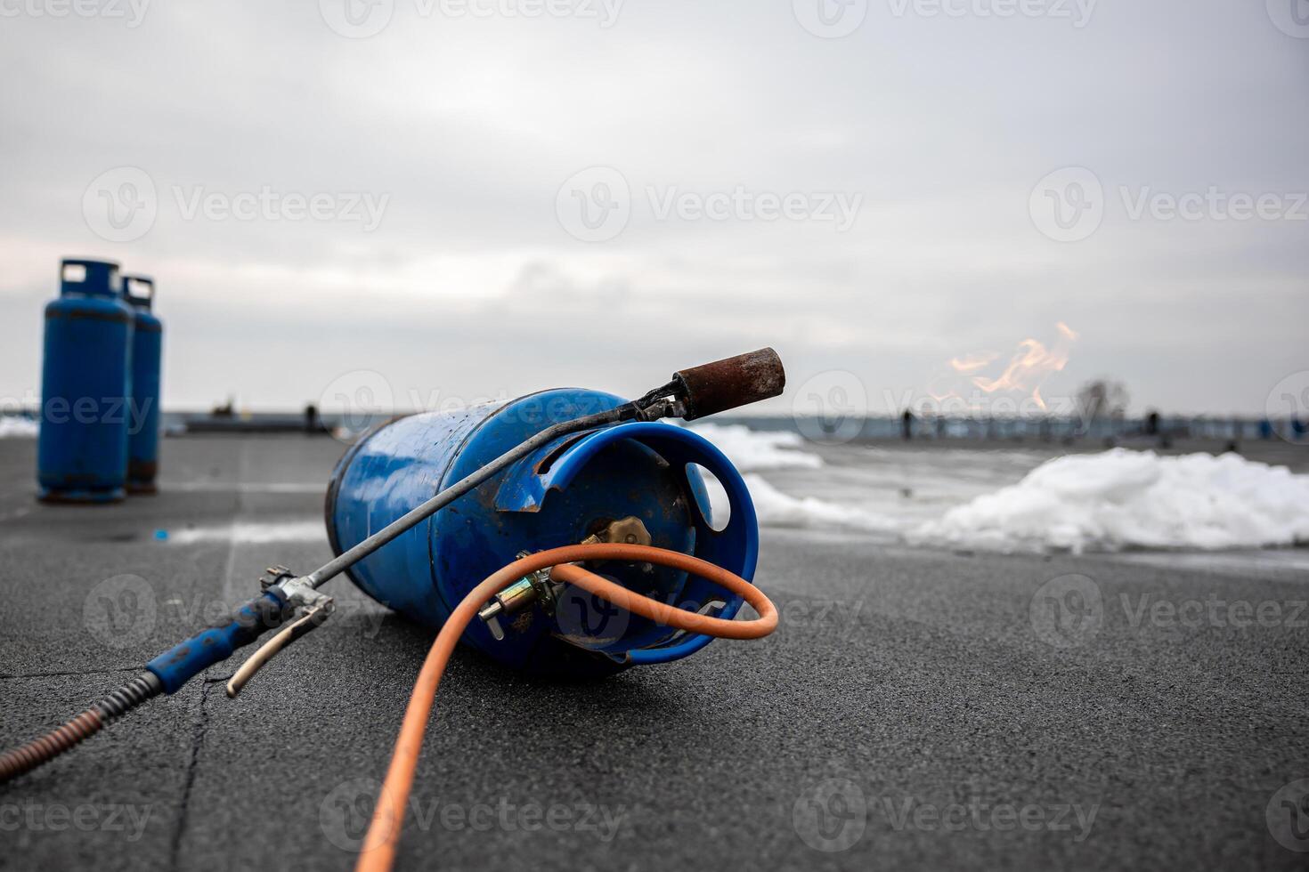 gas torch tool lying on new roofing surface with propane tank and hose, essential equipment for construction workers for melting and sealing tar on flat roof photo