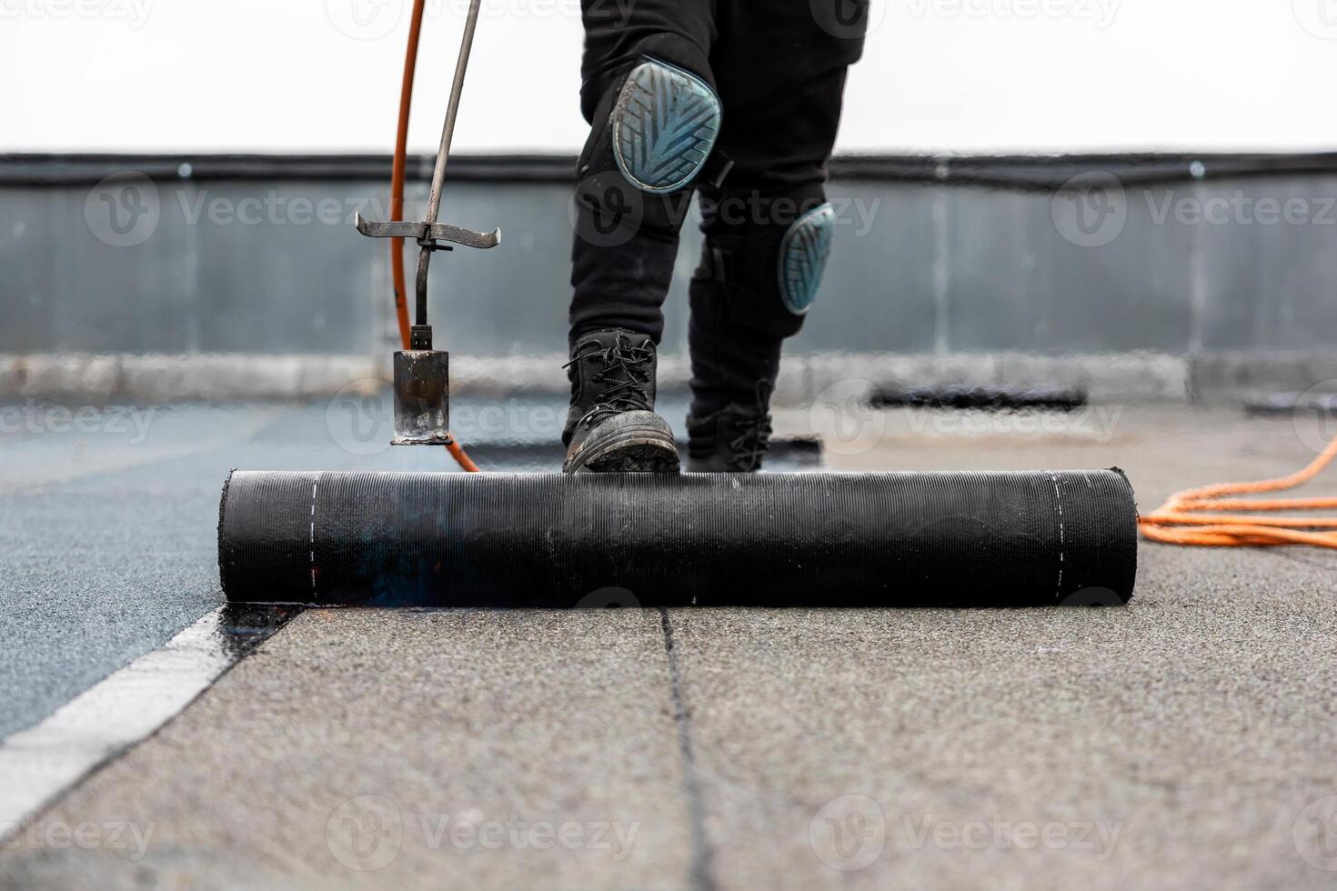 professional roofer applying bitumen roll on flat roof with a gas burner at a modern construction site photo