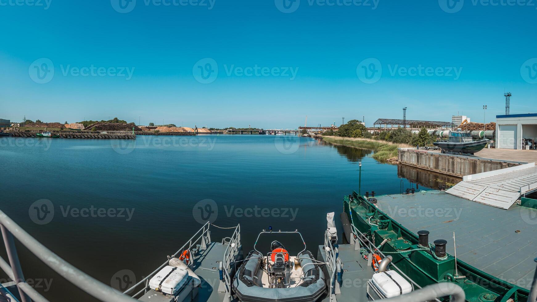 View from a Military Patrol Boat Navigating River with Industrial Port Horizon and Blue Sky photo