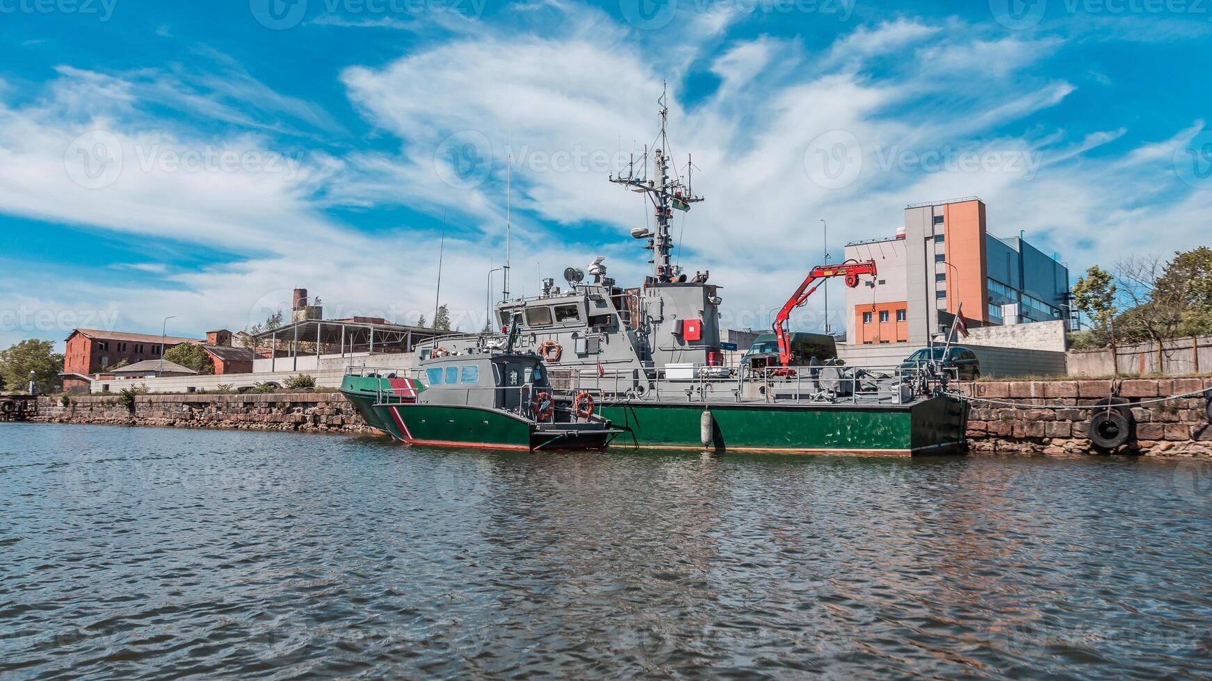Naval patrol boat moored at the city dock with industrial equipment on board against a backdrop of urban buildings and a clear sky photo